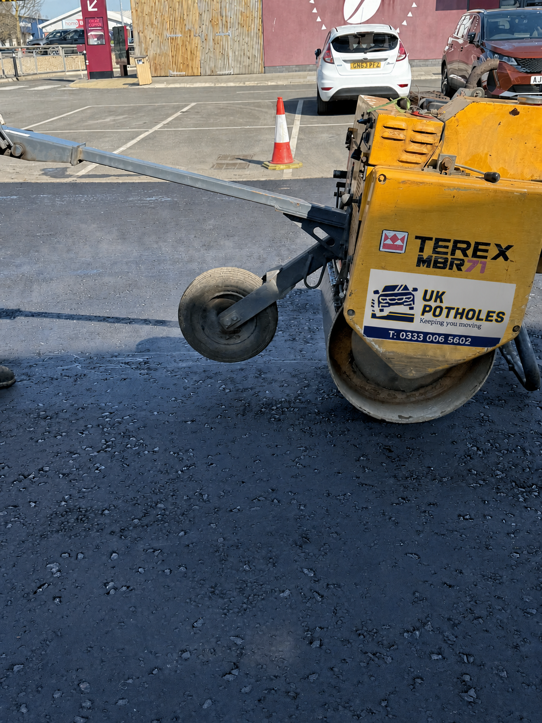 UK Potholes pedestrian roller compacting freshly laid tarmac surface course on a commercial car park, achieving the specified air void content
