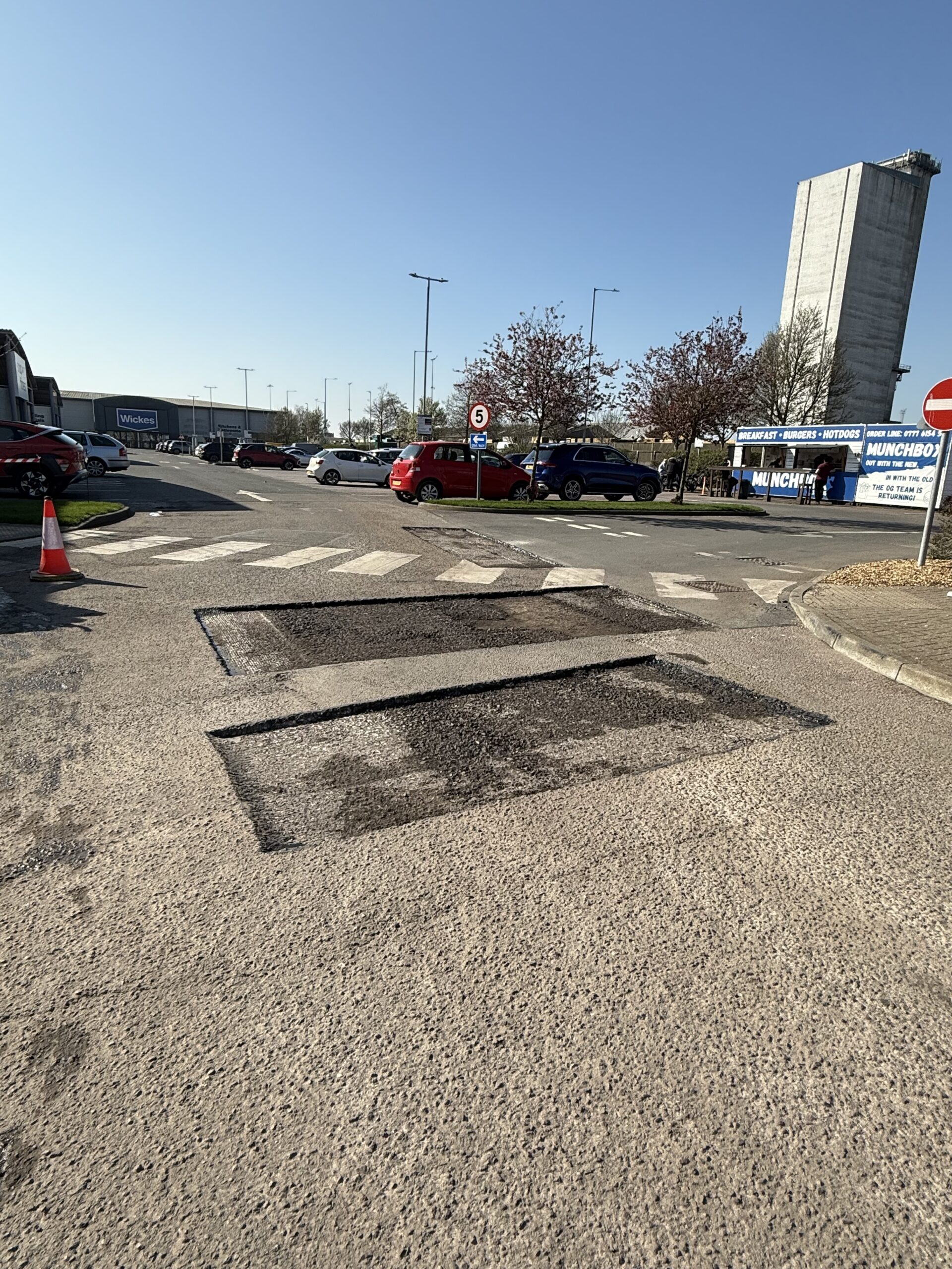 Operative using a pedestrian roller on a hot tarmac surface with steam rising, compacting the asphalt wearing course on a retail park resurfacing project