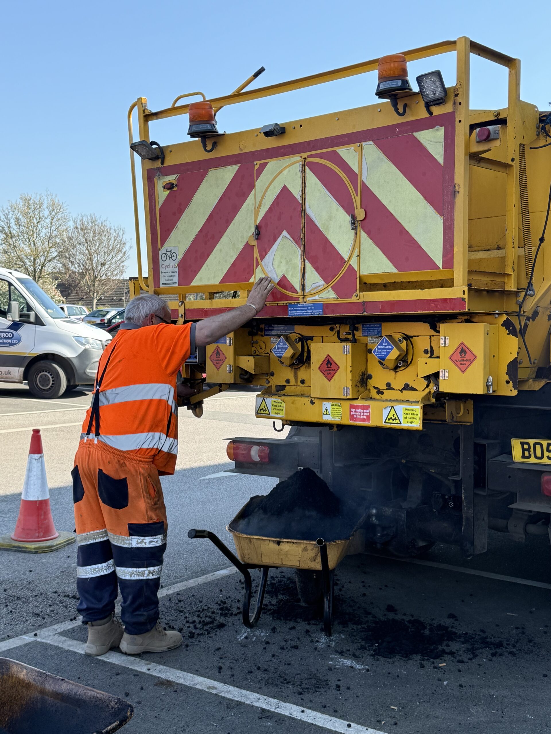 UK Potholes operative hand-raking hot tarmac asphalt to a consistent depth on a retail park car park resurfacing project