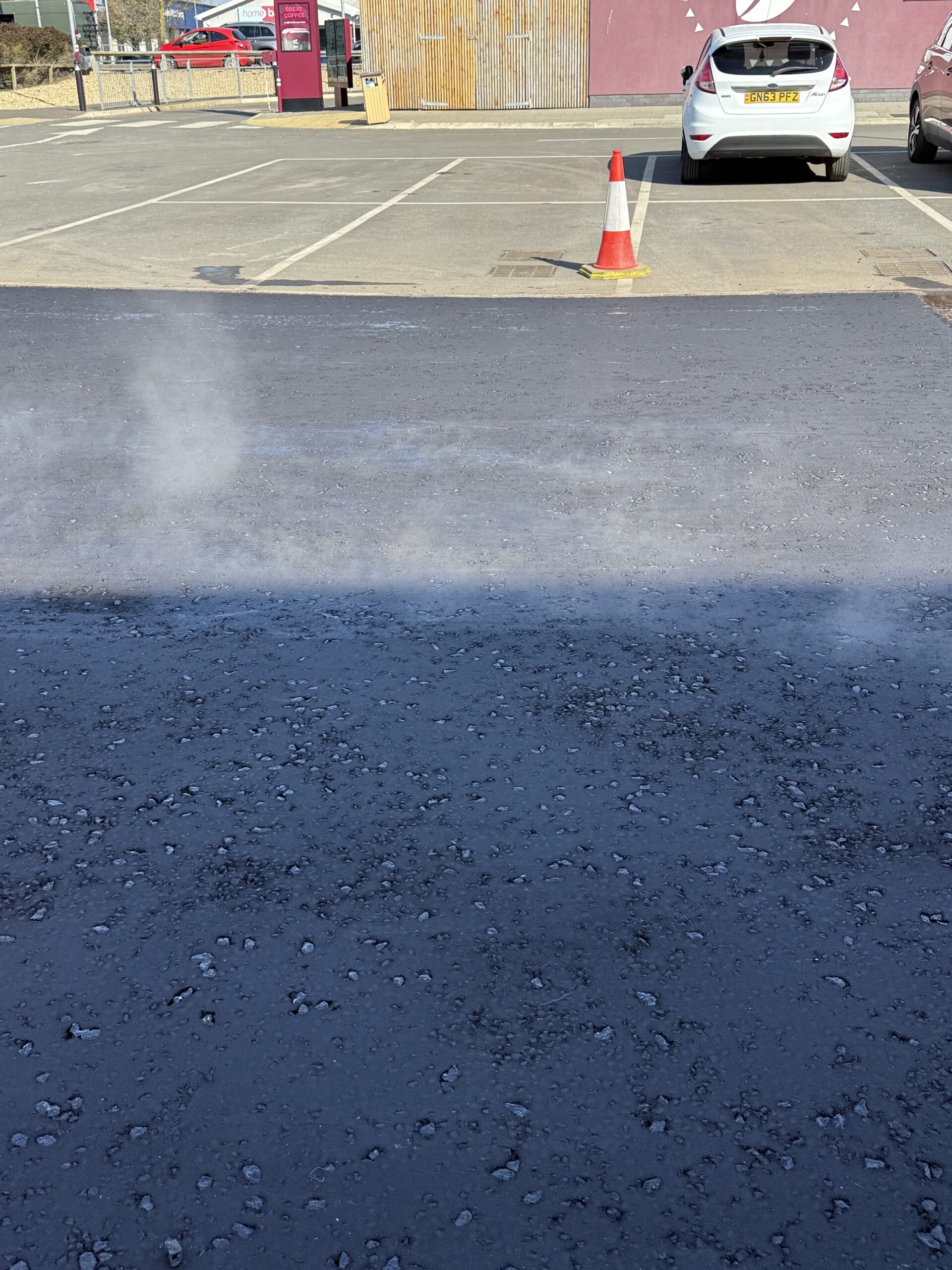 Road sweeper vehicle cleaning a commercial car park surface prior to tarmac resurfacing works, removing loose debris and fine material