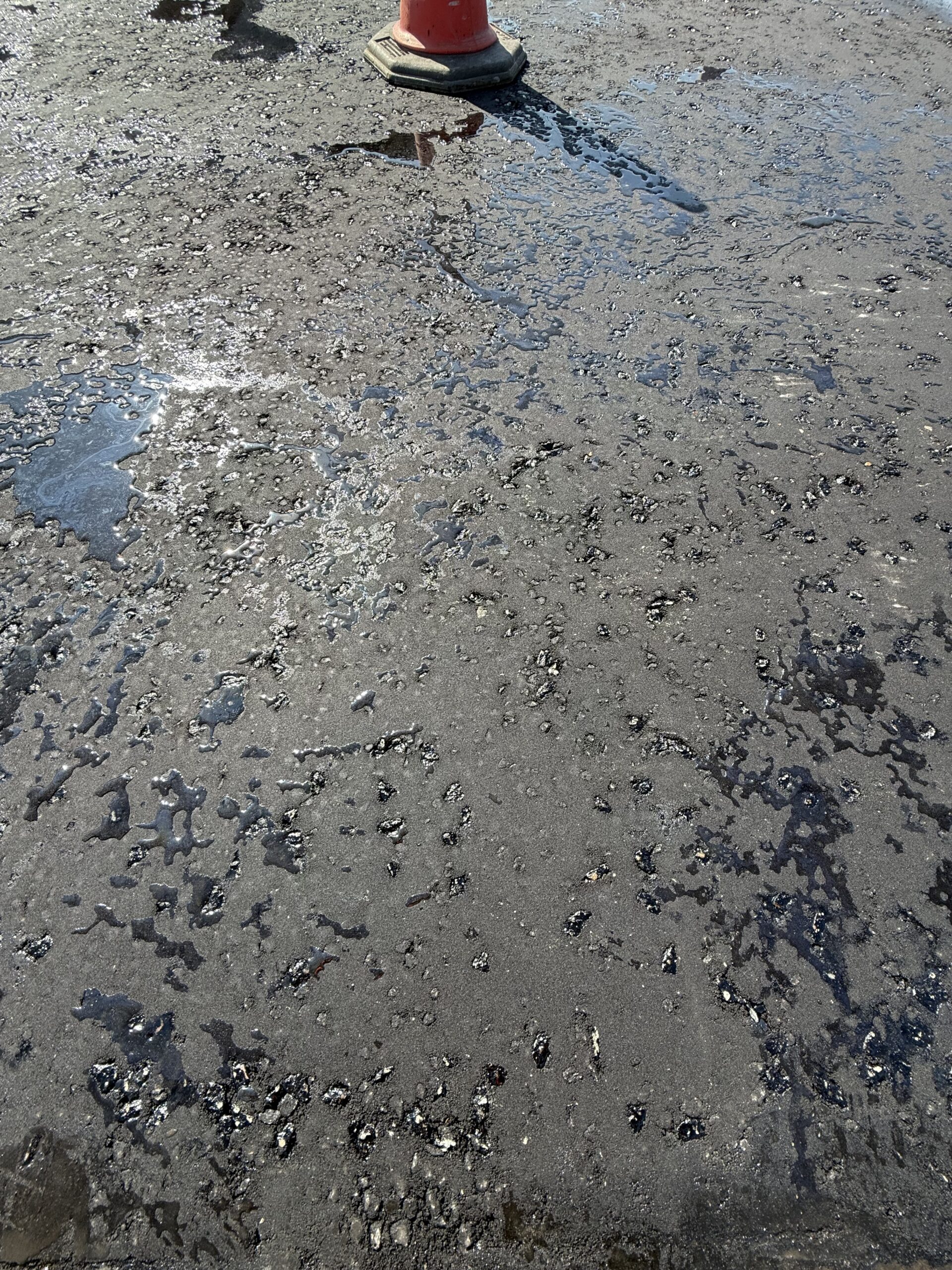 Close-up of correctly applied bitumen emulsion tack coat on a car park surface, showing the bond coat breaking from brown emulsion to black residual binder before tarmac is laid